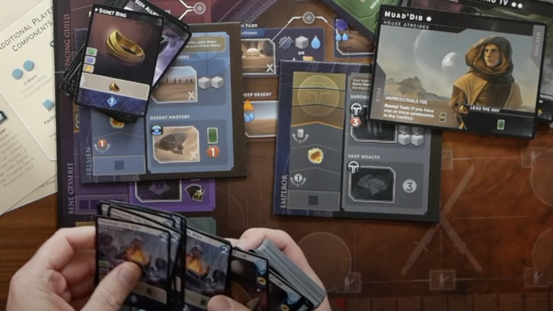 Hands hold cards above a table strewn with Dune: Imperium - Uprising cards