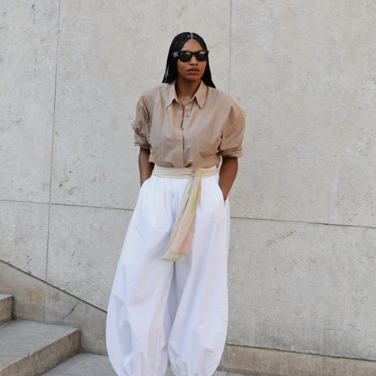 An image of an influencer wearing black sunglasses, a beige top and white cotton balloon trousers