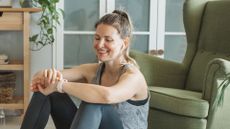Woman checking fitness tracker watch, sat on floor at home in living room wearing workout clothes, after doing good morning exercise with weights