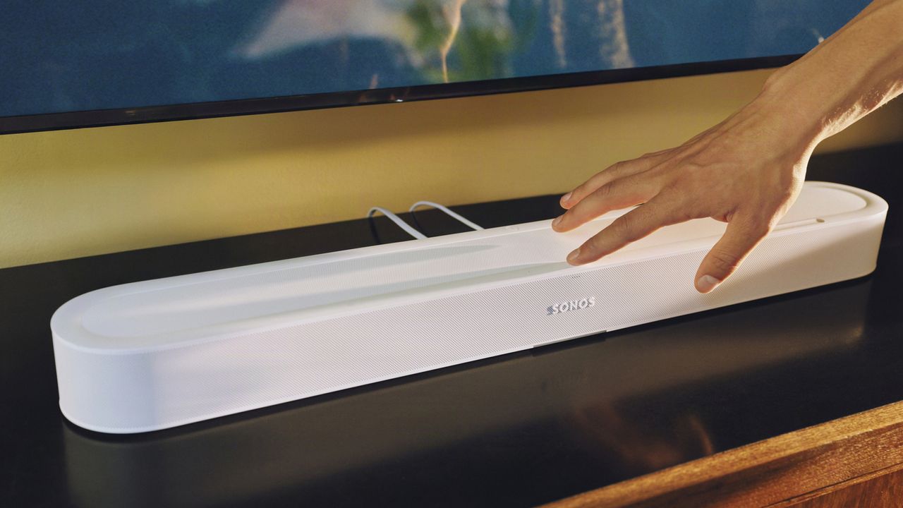 A hand reaching out for a white Sonos Beam Ultra soundbar below a TV
