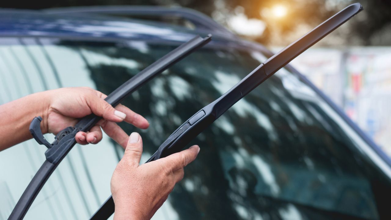 A pair of hands compairing the size of two windshield wipers