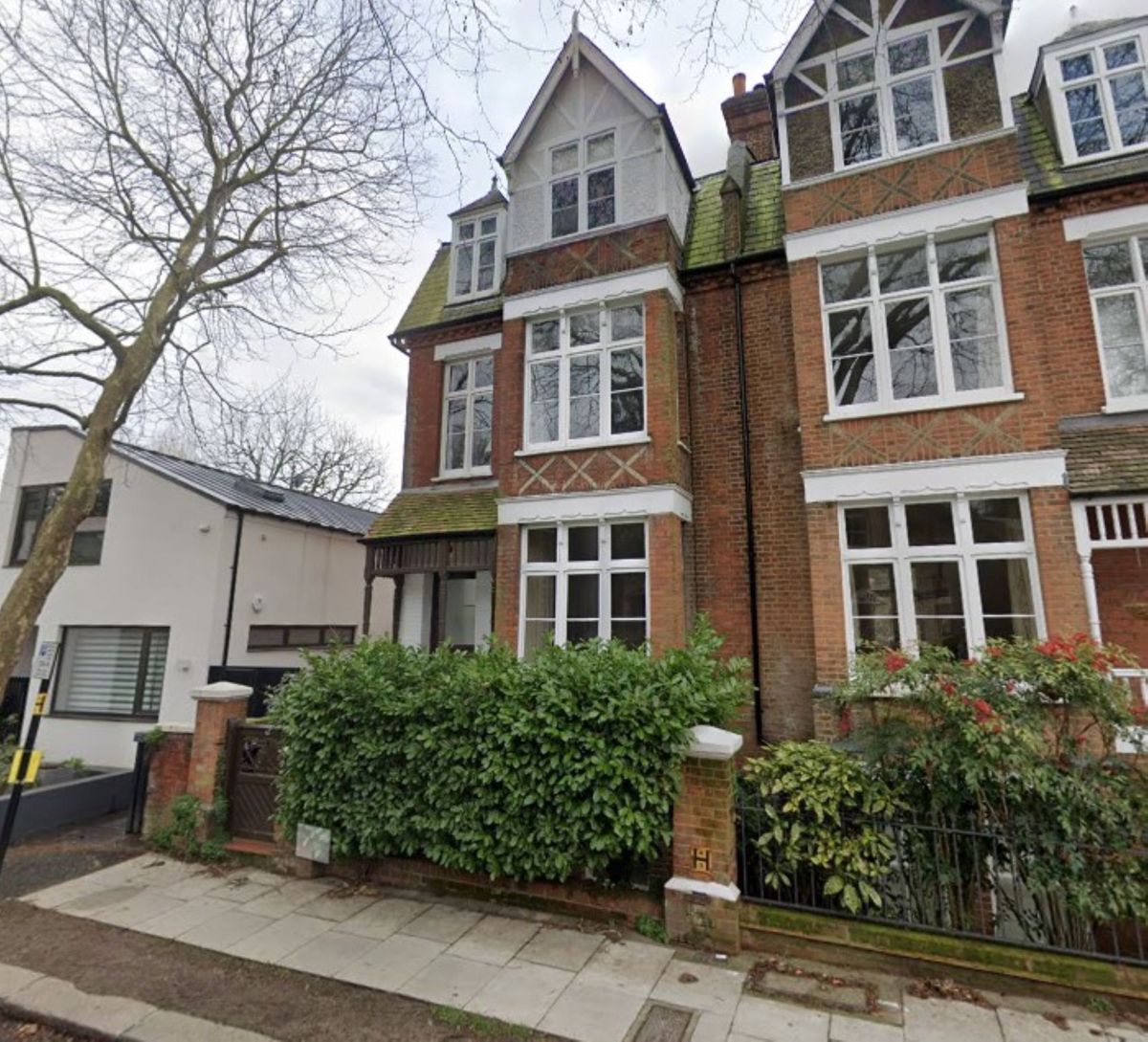 A brick semi-detached, three tiered house with triangular roof and hedged front garden