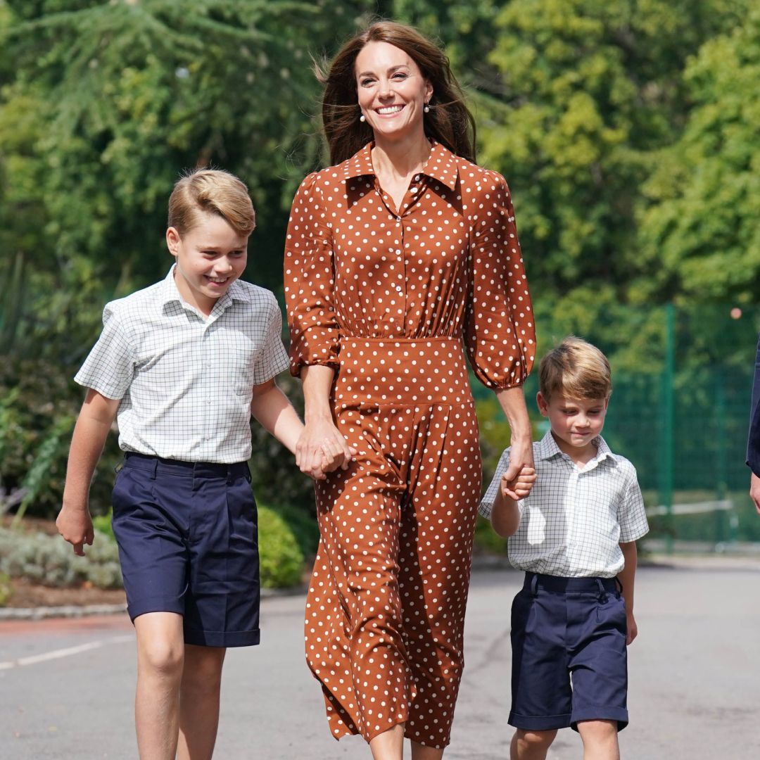 Princess Kate wearing a brown dress holding hands with Prince George and Prince Louis in school uniform