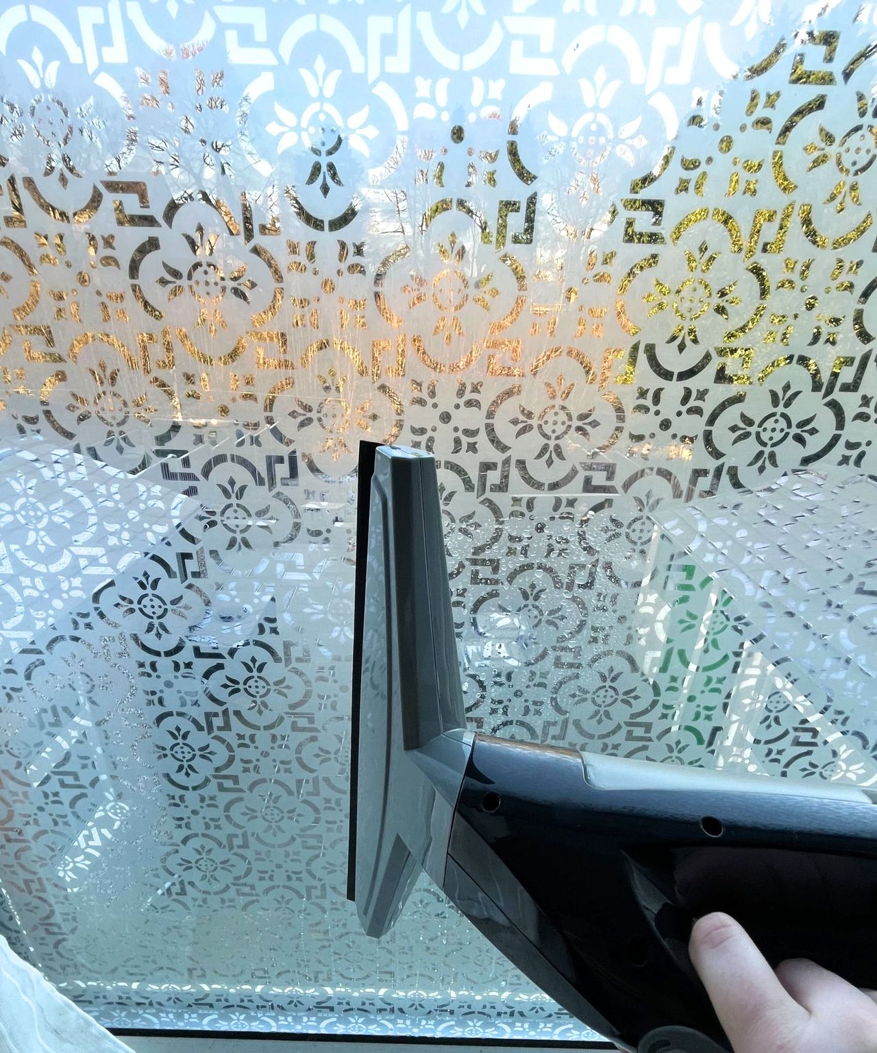 Cleaning a pattered bathroom window with a spray bottle and a window vacuum