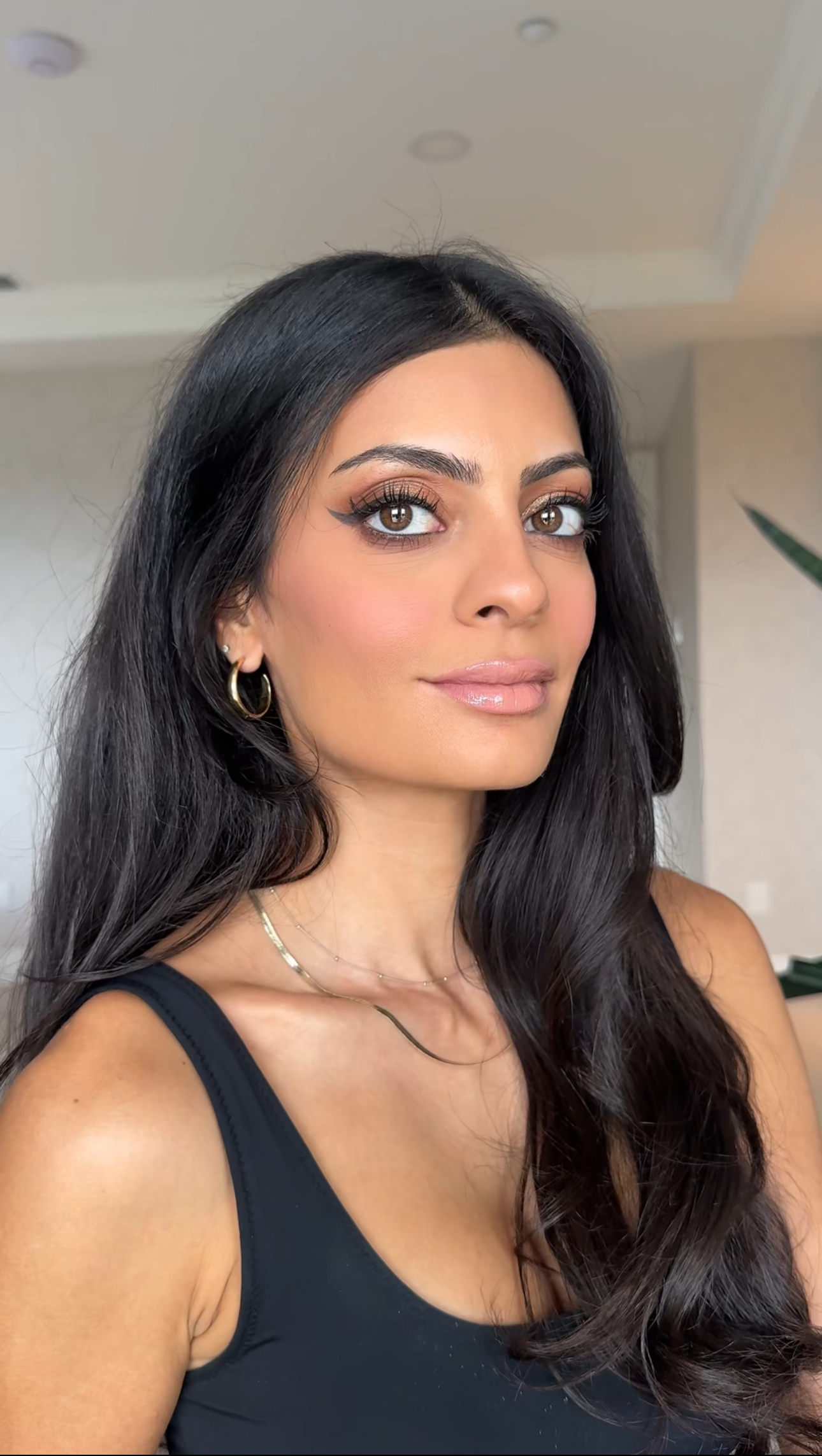 a woman with dark hair and eyes in a black tank top and gold necklace