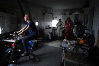 Anastasiya Stepanova exercises while fellow Mars 160 crewmembers prepare for an extravehicular activity.