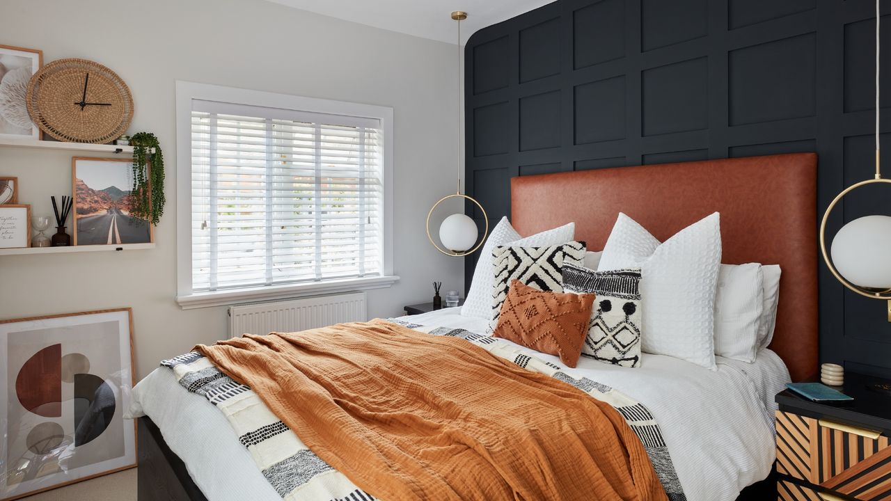 A small bedroom with a black panelled wall and two pendant lights on either side of the bed with a brown leather headboard