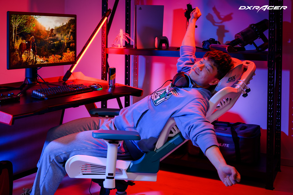 A man reclines happily in a DXRacer Air Series chair in front of a desk with a gaming computer. The room is lit with red RGB lights.