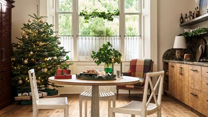 Open plan kitchen decorated for Christmas with a christmas tree in one corner and a burl wood kithen and circular dining table in the center