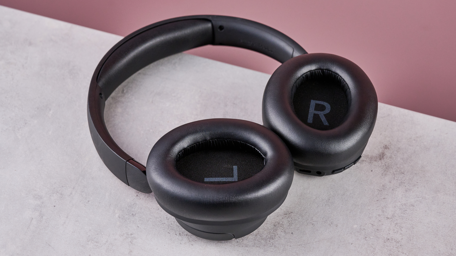 Amazon Basics Hybrid Active Noise Cancelling Headphones on a gray surface, with a pink background, showing the inside of the earcups