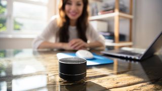 A businesswoman working from home and smiling at a smart speaker