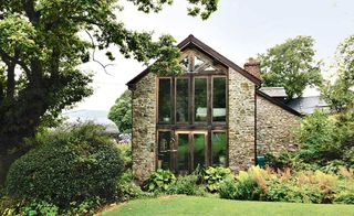 a large stone-built farmhouse in the countryside, surrounded by trees, hedges, and a manicured garden