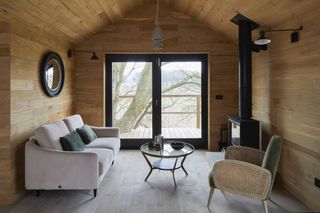 cabin style living room with log burner, gray couch, cane armchair, mirror, doors out onto raised patio