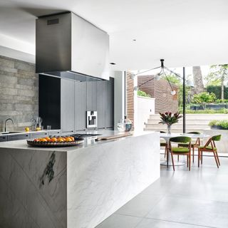 Kitchen with grey tiled concrete floor, large marbled kitchen island, floor to ceiling glass doors to the patio and garden