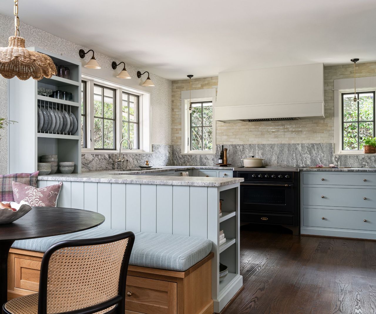 A kitchen with a peninsula island, a dining nook, blue cabinets and tiled walls