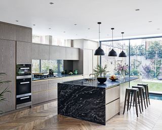 A black marble kitchen island below three pendant lights in front of gray cabinets