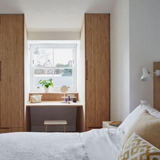 bedroom with fitted wardrobes and desk built-in around a window with a bed in the foreground