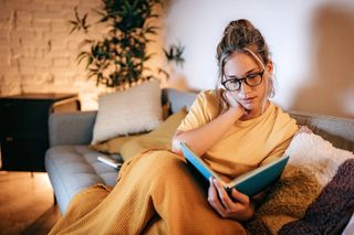 A woman wears blue light blocking glasses to reads a book after waking up in the middle of the night