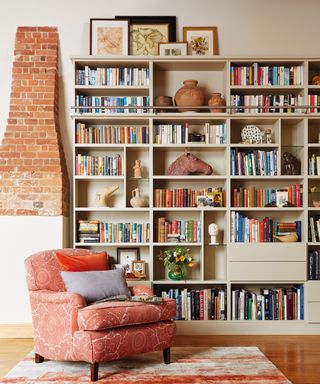 Large floor to ceiling bookshelf, orange armchair, patterned rug, brick chimney