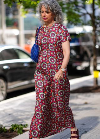 A NYFW guest wearing white earrings with a dark red patterned La DoubleJ short sleeve midi dress, with a dark blue feathered bag.