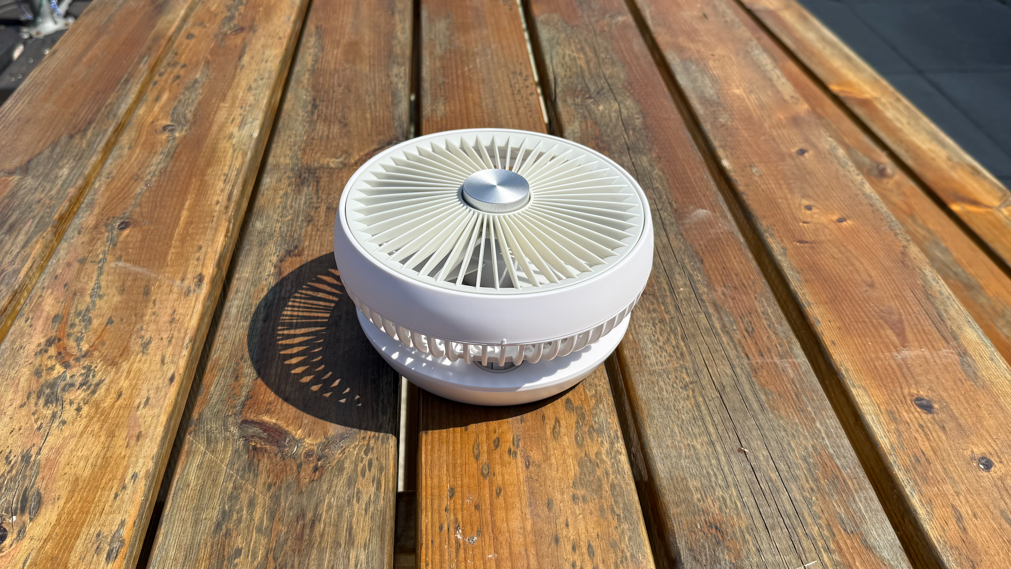 The Dimplex Rechargeable Cordless Desk Fan on a wooden bench table with the fan folded down for travel