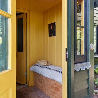 interior of house porch with panelled walls painted yellow, and a storage bench with a cushion