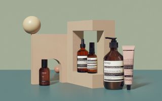 Aesop skincare in brown bottles displayed on blush wooden stand, with sphere on one corner