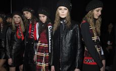 Models backstage wearing variations of black and red skirts, jackets and headwear