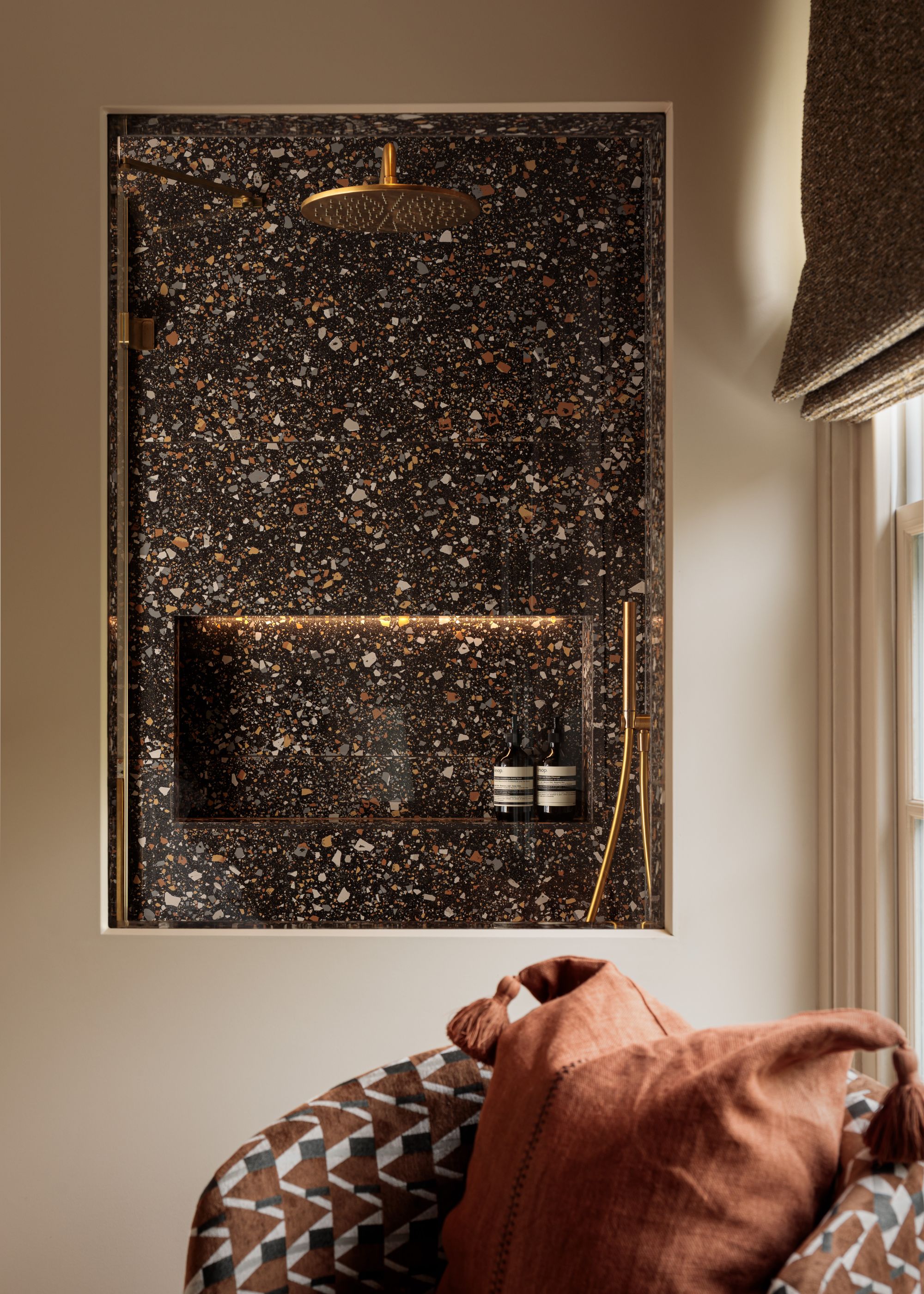 A bathroom painted beige with a view from the internal window looking into the shower room with golden features