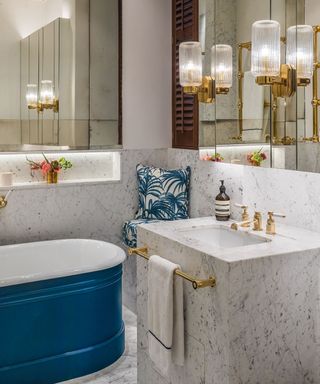 A luxury bathroom with marble basin, fluted glass and brass scone lights and blue cast iron bath