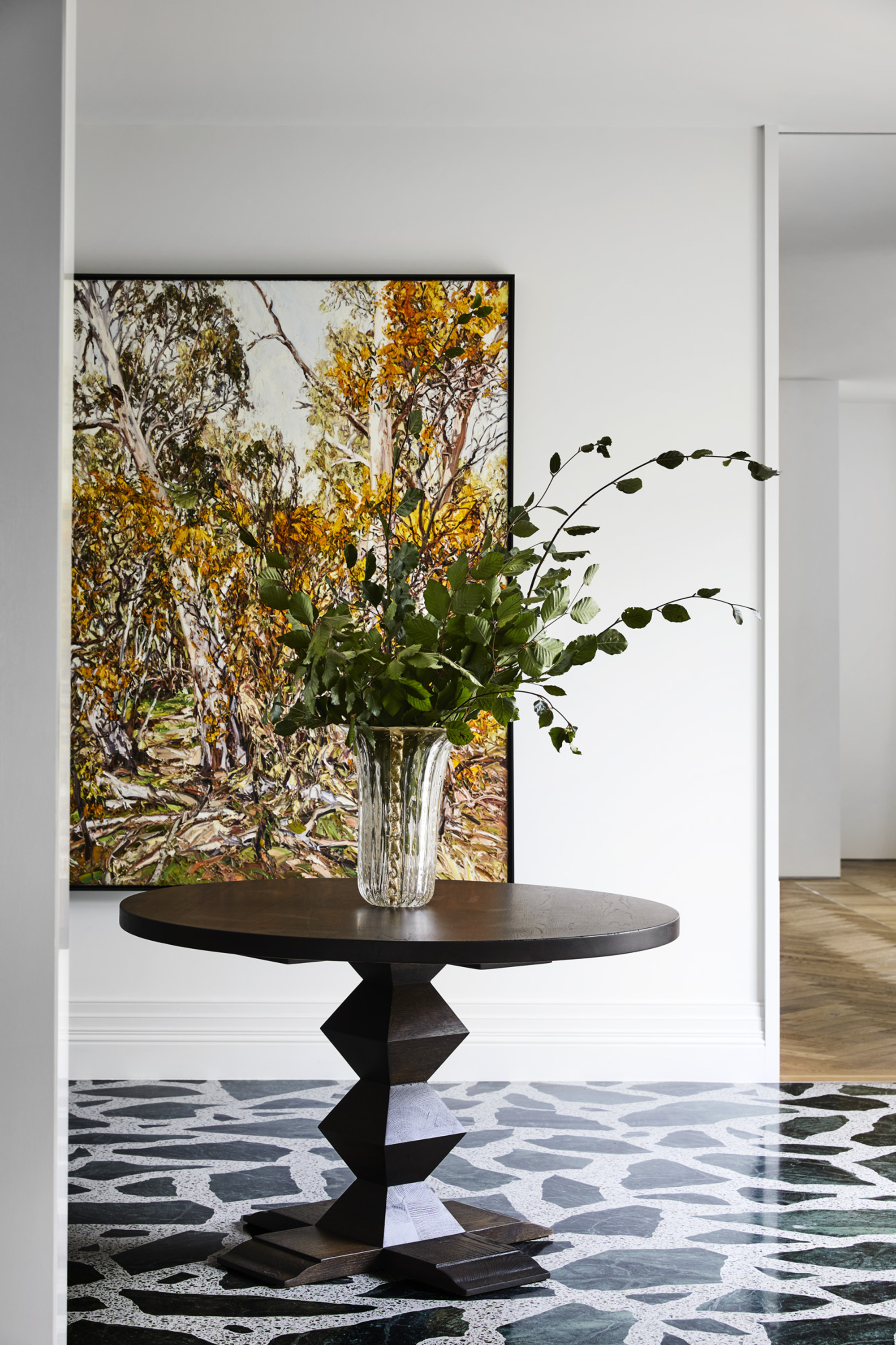entryway with green palladiana flooring, a round timber table with a vase of flowers, and a large artwork on the wall