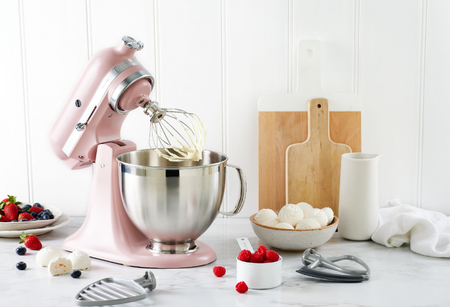 Pink KitchenAid standmixer on a kitchen counter with chopping boards, fruits and cake ingredients
