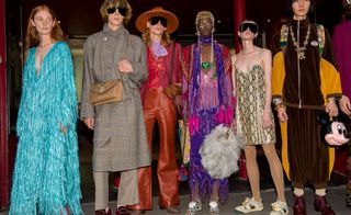 Models wear blue dress, grey trench coat, red suit, purple dress, snake dress and brown and orange tracksuit