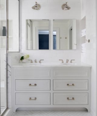 A bathroom with white double vanity, statuary herringbone tiles and statuary-clad shower