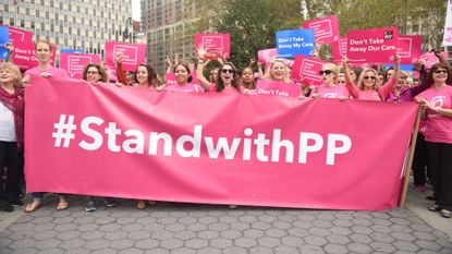 Protestors dressed in pink t-shirts holding aa banner that reads "#StandwithPP"