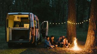 Group of campers around a campfire by a camper van, at night