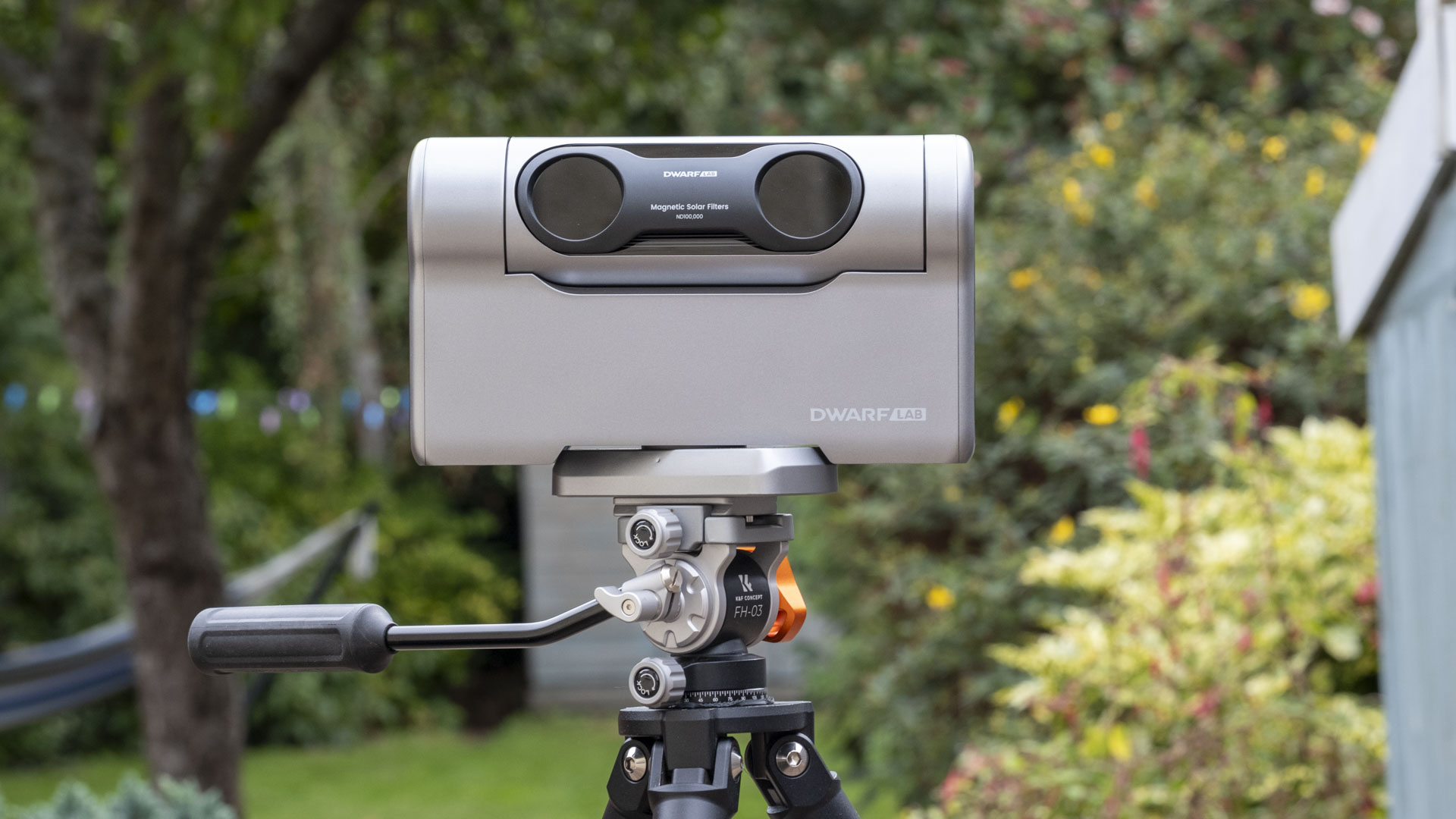 The Dwarf III smart telescope photographed in a garden, showing the front of the device with the solar filter attached
