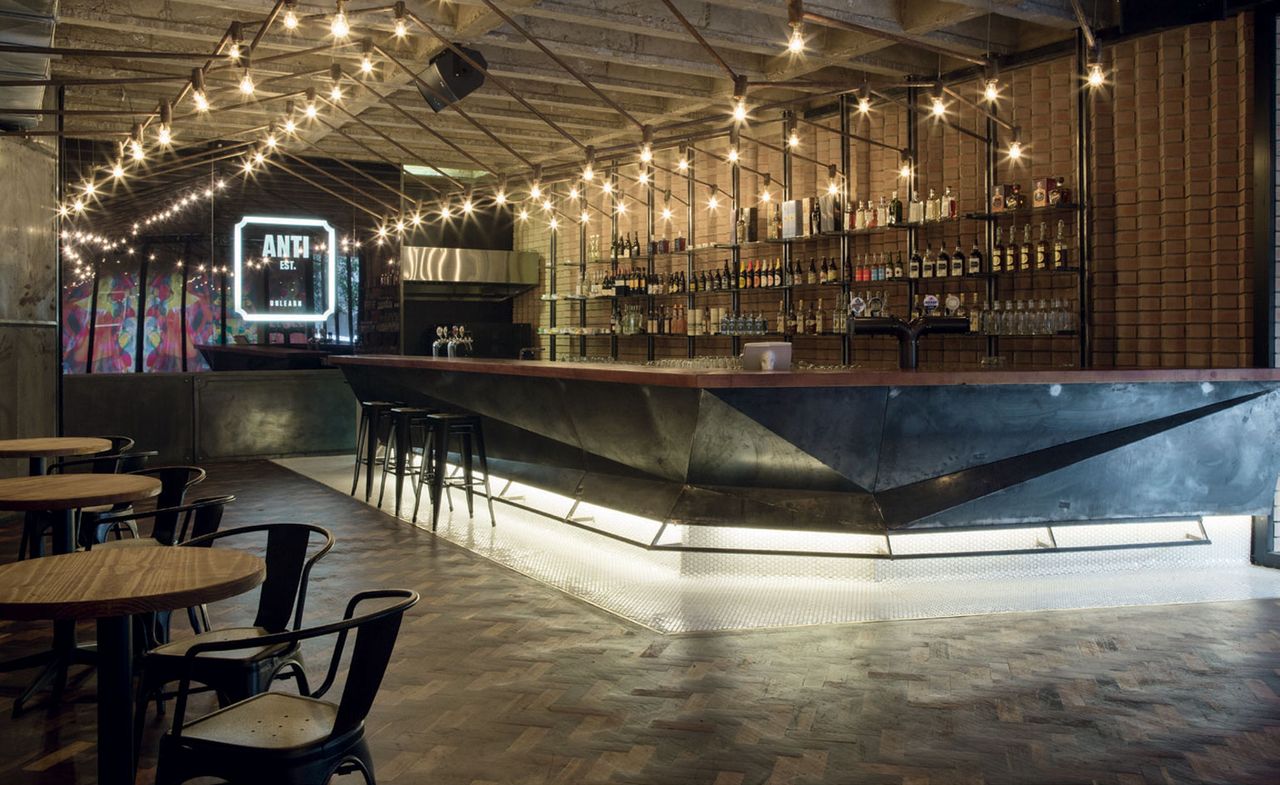 Inside Anti Est bar in Johannesburg. There are many wooden tables with black chairs and the lighting gives a great atmosphere.