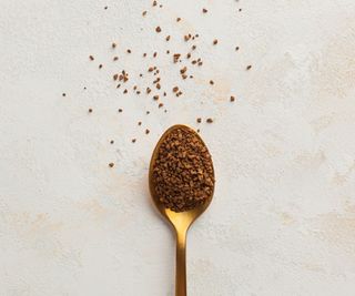 Gold teaspoon with instant coffee on it and some scattered on the countertop