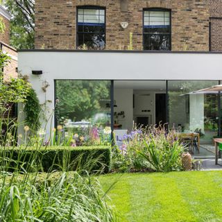 Natural hedge row border dividing green grass lawn from patio seating area next to house in garden