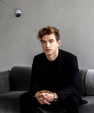 Interior designer Jeremiah Brent sat on a gray couch against a gray wall