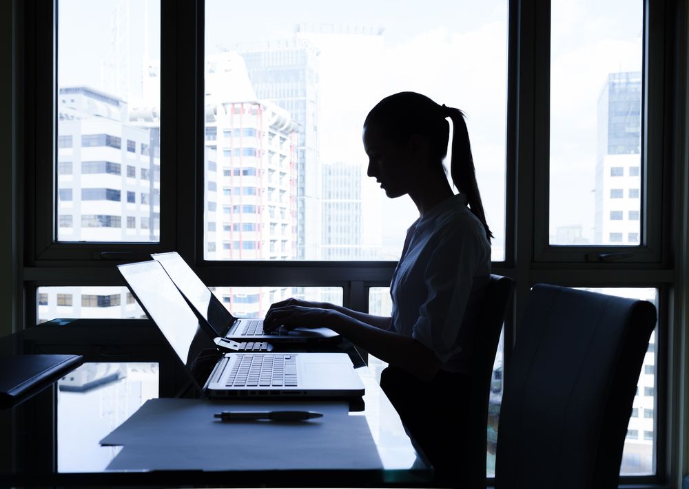 Silhouette of a woman sitting at a desk in front of a computer