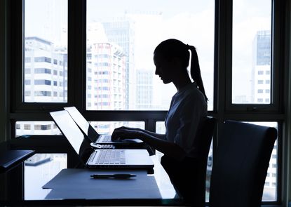 Silhouette of a woman sitting at a desk in front of a computer