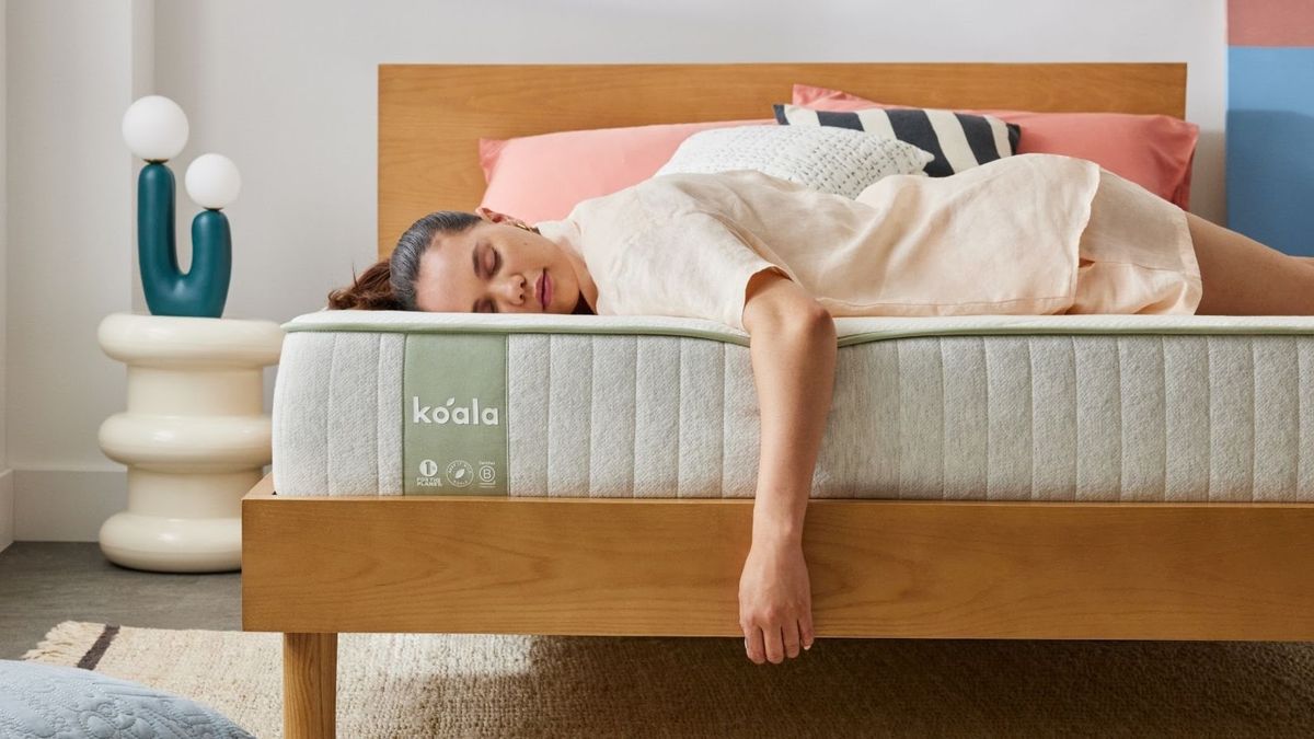 Koala SE mattress on a bed frame, with a person laying on the bed, one arm dangling from the end, showing edge support