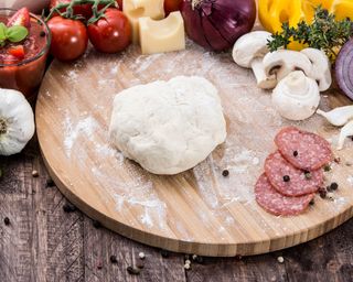 Homemade pizza dough on wooden background with other pizza ingredients