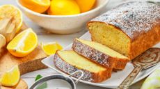 low fat lemon drizzle on a board dusted with icing sugar and surrounded by fresh wedges of lemon
