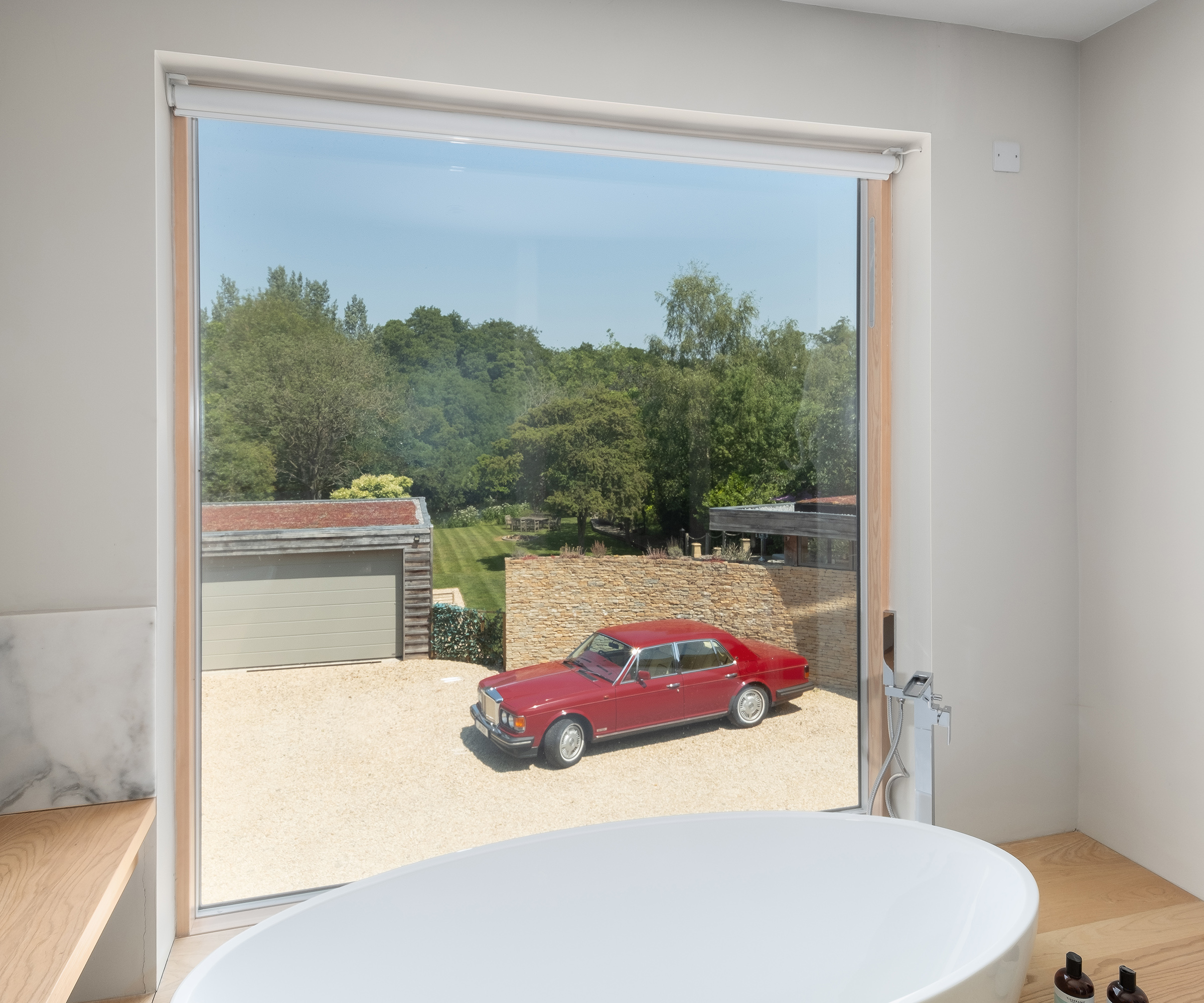 View out of a picture window into a gravel driveway with red car