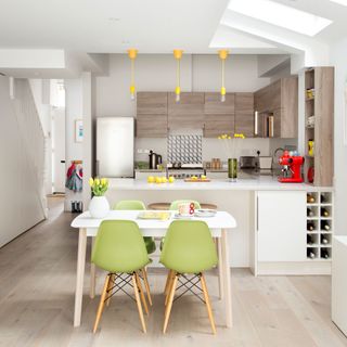 kitchen and dinning area with white wall white counter wooden cabinets and green chairs