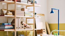 IKEA PS shelving unit decorated with books, files, and trinkets, against a yellow and white wall, with a blue floor lamp.