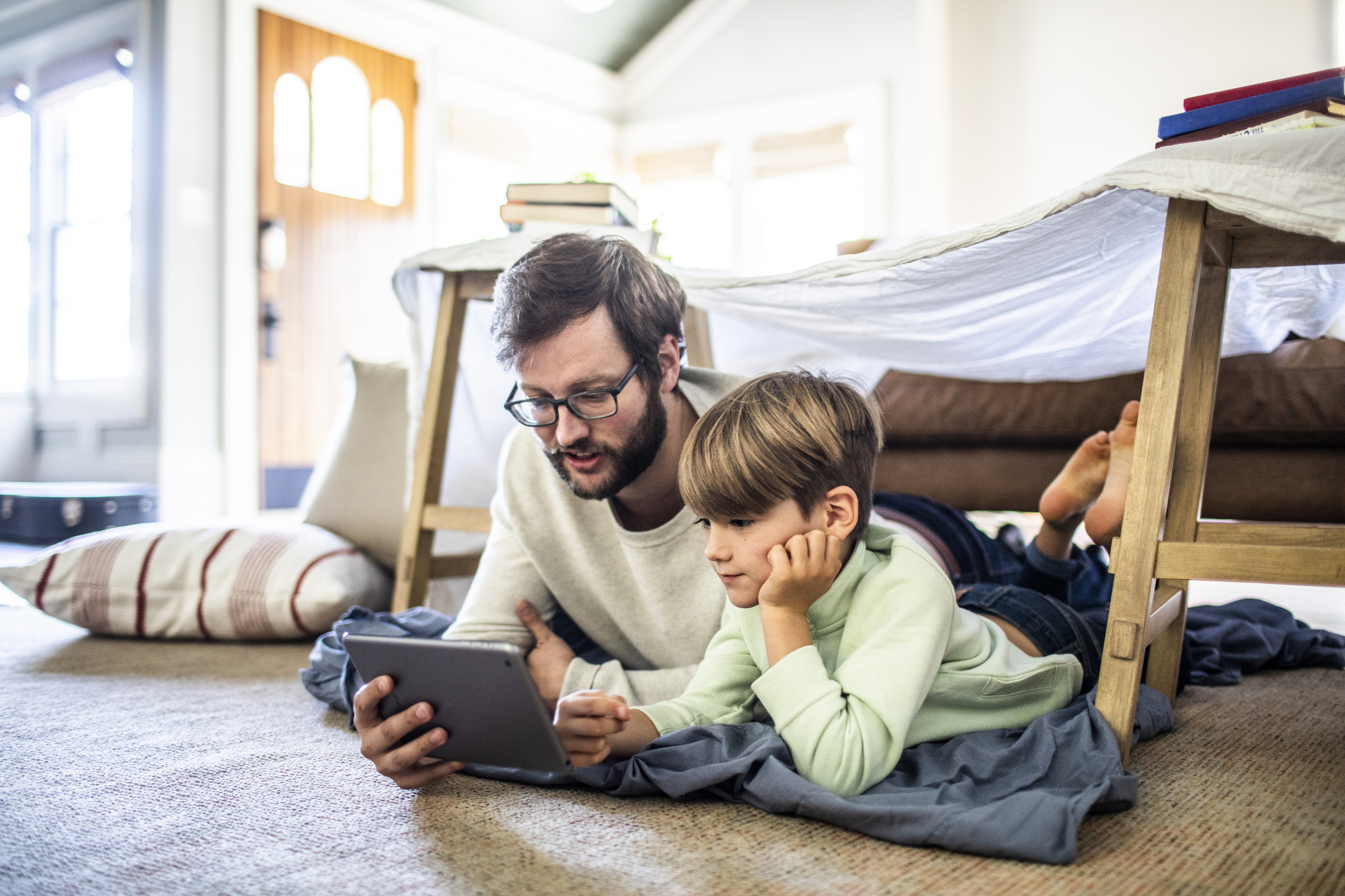 Father and son watching digital tablet in homemade fort
